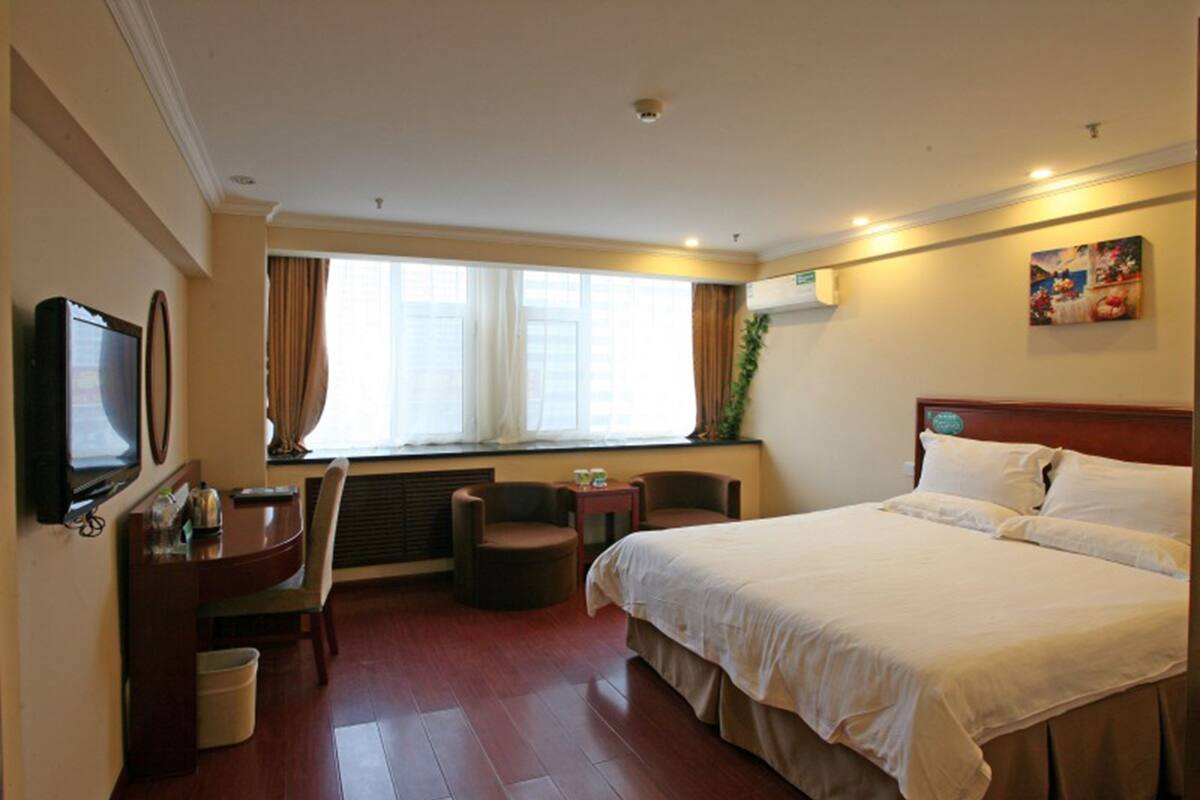 Ein Hotelzimmer mit einem Bett, einem Schreibtisch mit Stuhl, einem Fernseher und einem Fenster mit Vorhängen.