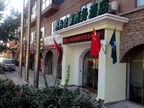 A hotel facade with a sign in a foreign language, a red flag, and a stone wall. - GreenTree Inn Beijing Changping District Beiqijia Future Science & Technology City Hotel (Beijing)