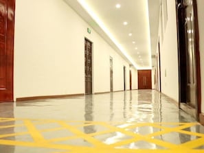 A long, well-lit hallway with a shiny floor, wooden doors, and a clean, modern design.