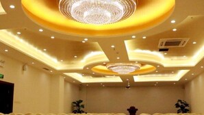 Une salle de conférence avec des rangées de chaises, un lustre central et des luminaires encastrés dans le plafond.