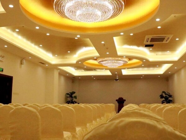 A conference room with rows of chairs, a central chandelier, and recessed ceiling lighting.