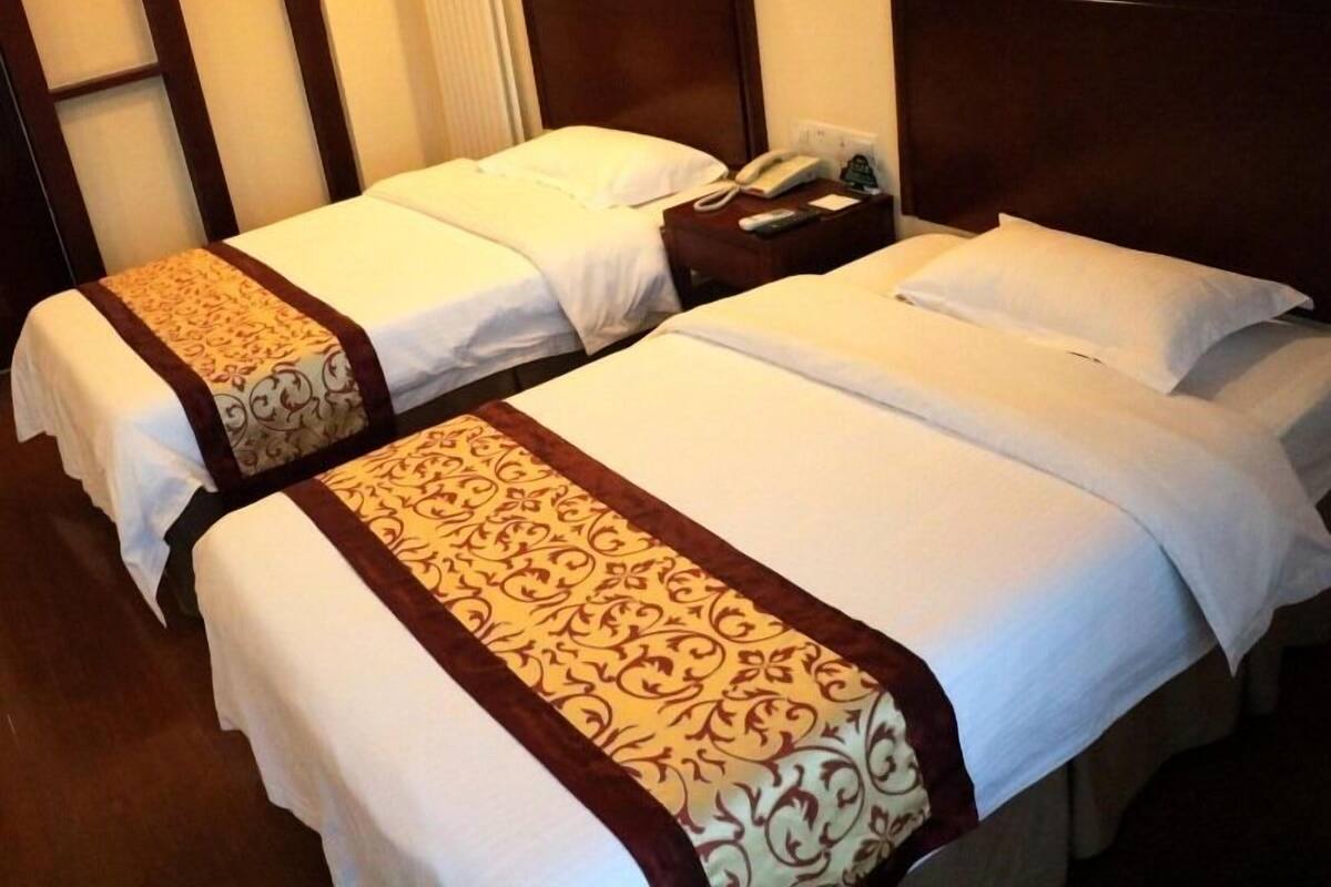 Deux lits jumeaux avec du linge de lit blanc et des bordures décoratives marron, une table de chevet avec un téléphone et un luminaire fixé au mur.