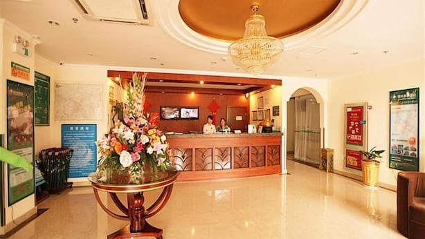 Un hall d’hôtel avec un comptoir d’accueil, un grand arrangement floral, un lustre et une carte affichée au mur.