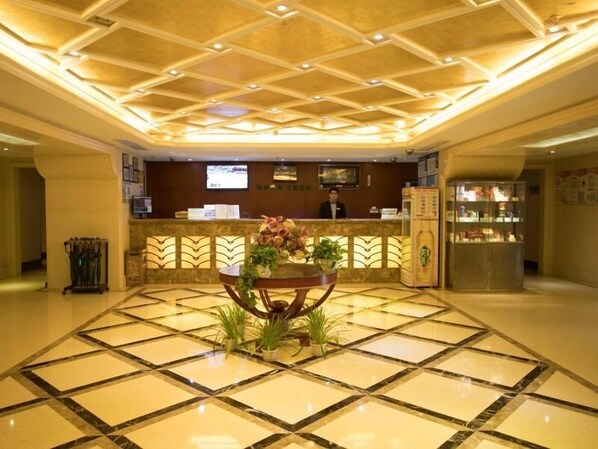 Un vestíbulo de hotel con una recepción, una mesa grande con plantas y un suelo de baldosas.