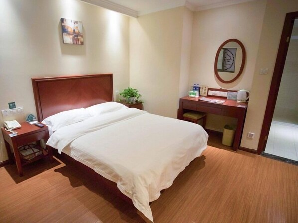 A hotel room with a wooden bed, a desk with a telephone and a plant, and a wall clock. - Greentree Inn Suzhou Station Hotel (Suzhou)
