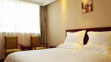 A hotel room with a large bed, two chairs, a small table, and a painting on the wall.