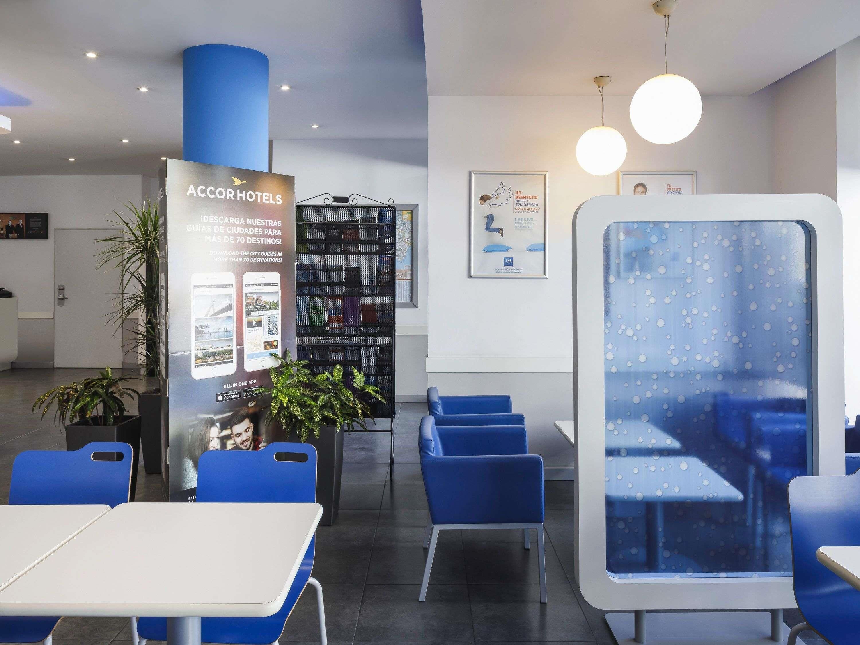 Zona de recepción de un hotel con una decoración azul y blanca, que incluye un mostrador de recepción, una sala de espera y un cartel grande que anuncia la app de AccorHotels.