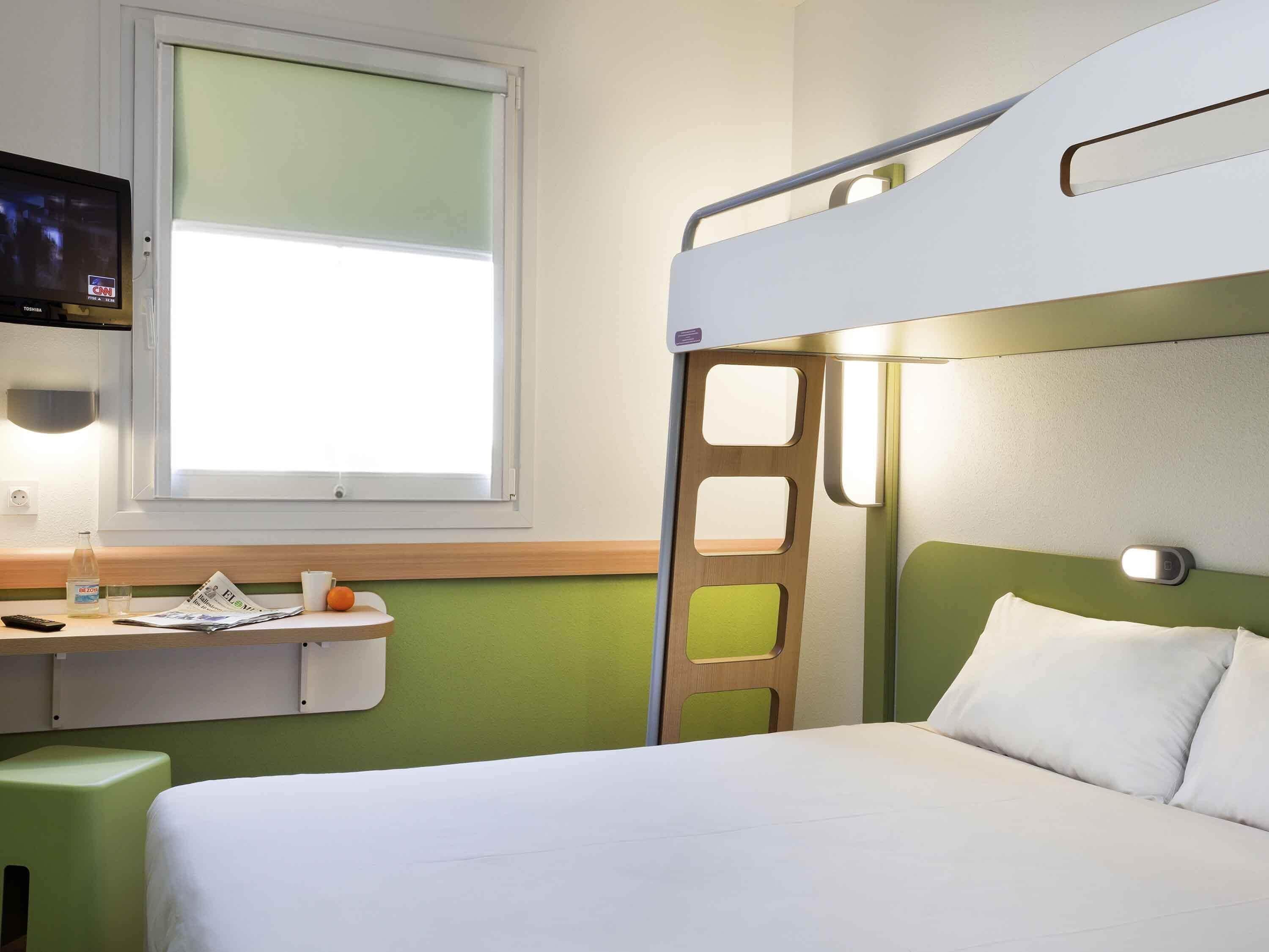 A bunk bed room with a desk, a TV, and a window.