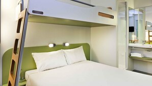 Een stapelbed met een groen hoofdbord, een nachtkastje met een lamp en een spiegel boven het bed.