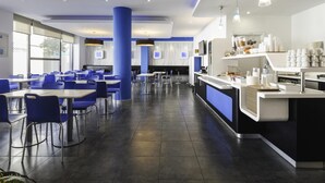 Een moderne eetruimte met blauwe stoelen, tafels en een centraal aanrecht met een drankstation.