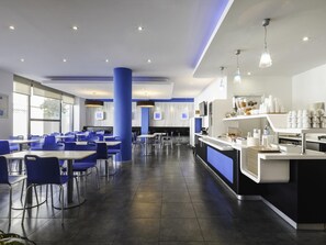 Un espace repas moderne avec des chaises et des tables bleues, ainsi qu’un comptoir central doté d’un espace dédié aux boissons.
