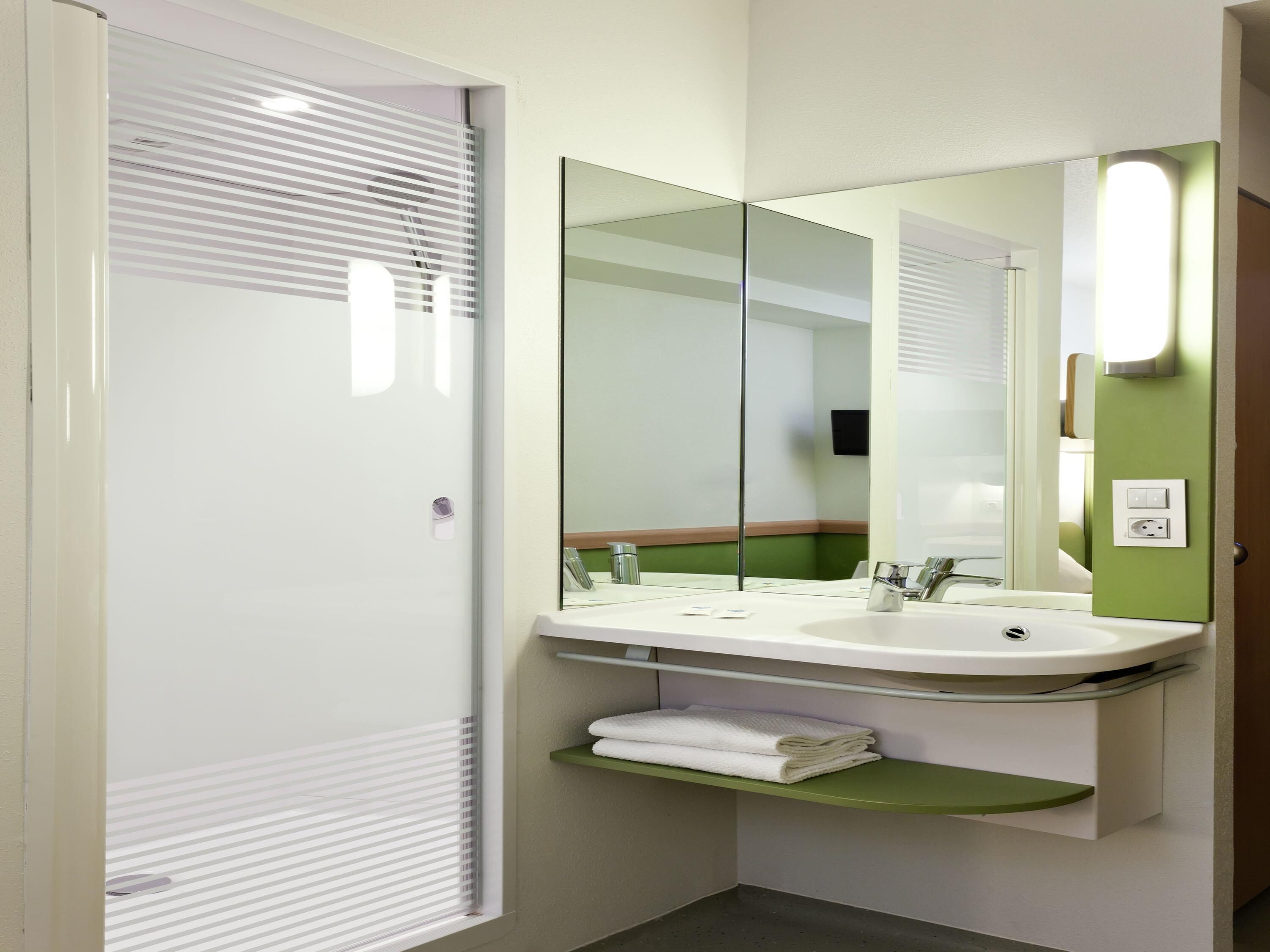A modern bathroom with a large mirror, white sink, and a towel rack.
