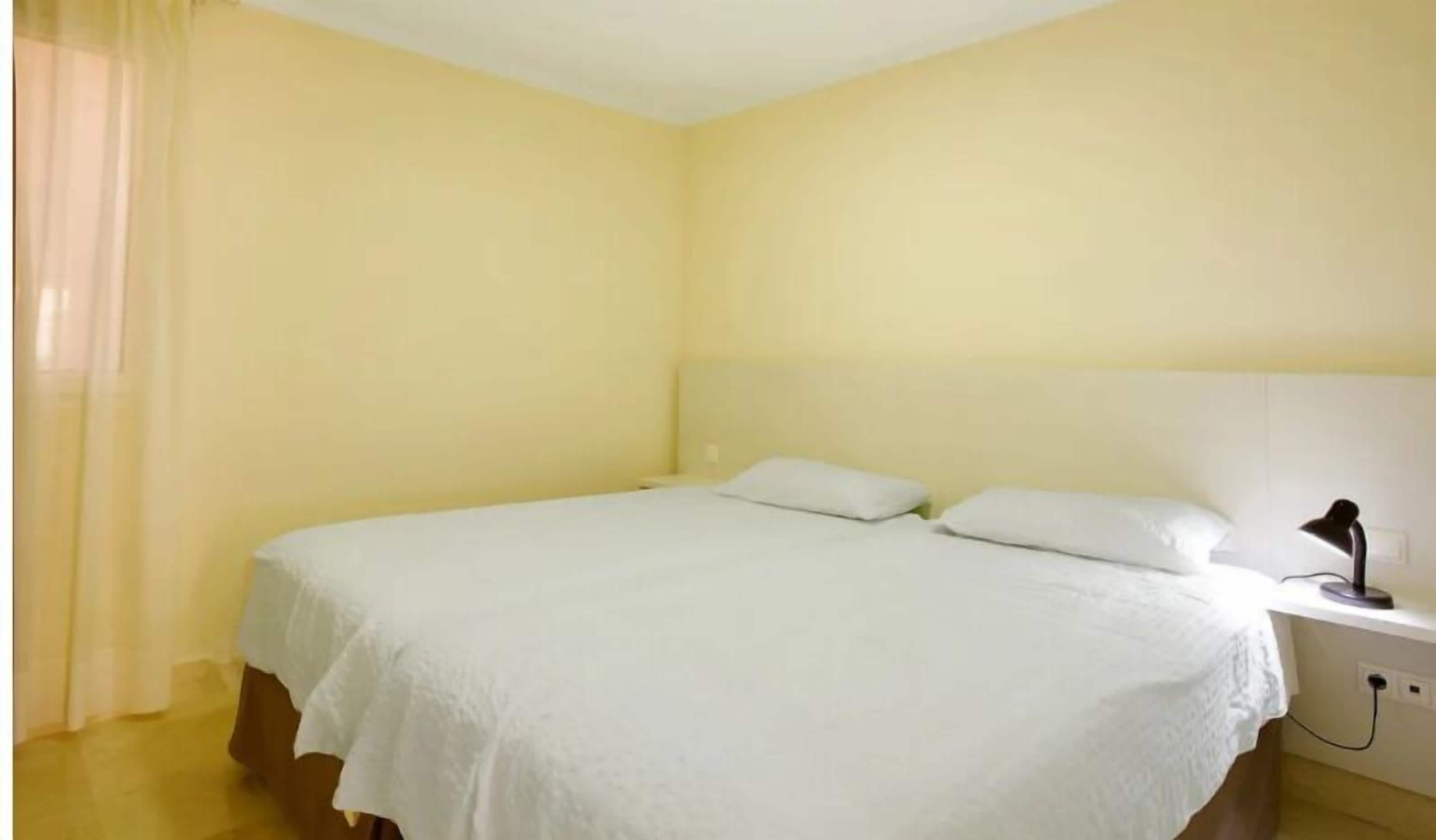 A simple, uncluttered bedroom with a bed, a nightstand, and a lamp.
