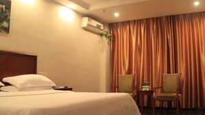 Habitación de hotel con cama, dos sillas, mesita de noche, equipo de aire acondicionado y una ventana grande con cortinas.