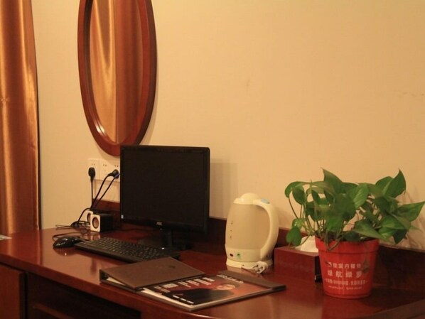 Un bureau en bois avec un ordinateur portable, un clavier, une souris, une machine à café, une plante en pot et un miroir accroché au mur.
