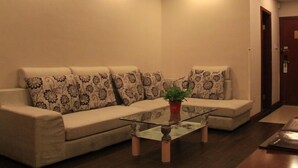 Una sala de estar con sofá color beige, cojines estampados, una mesa de centro de vidrio y una planta en maceta.
