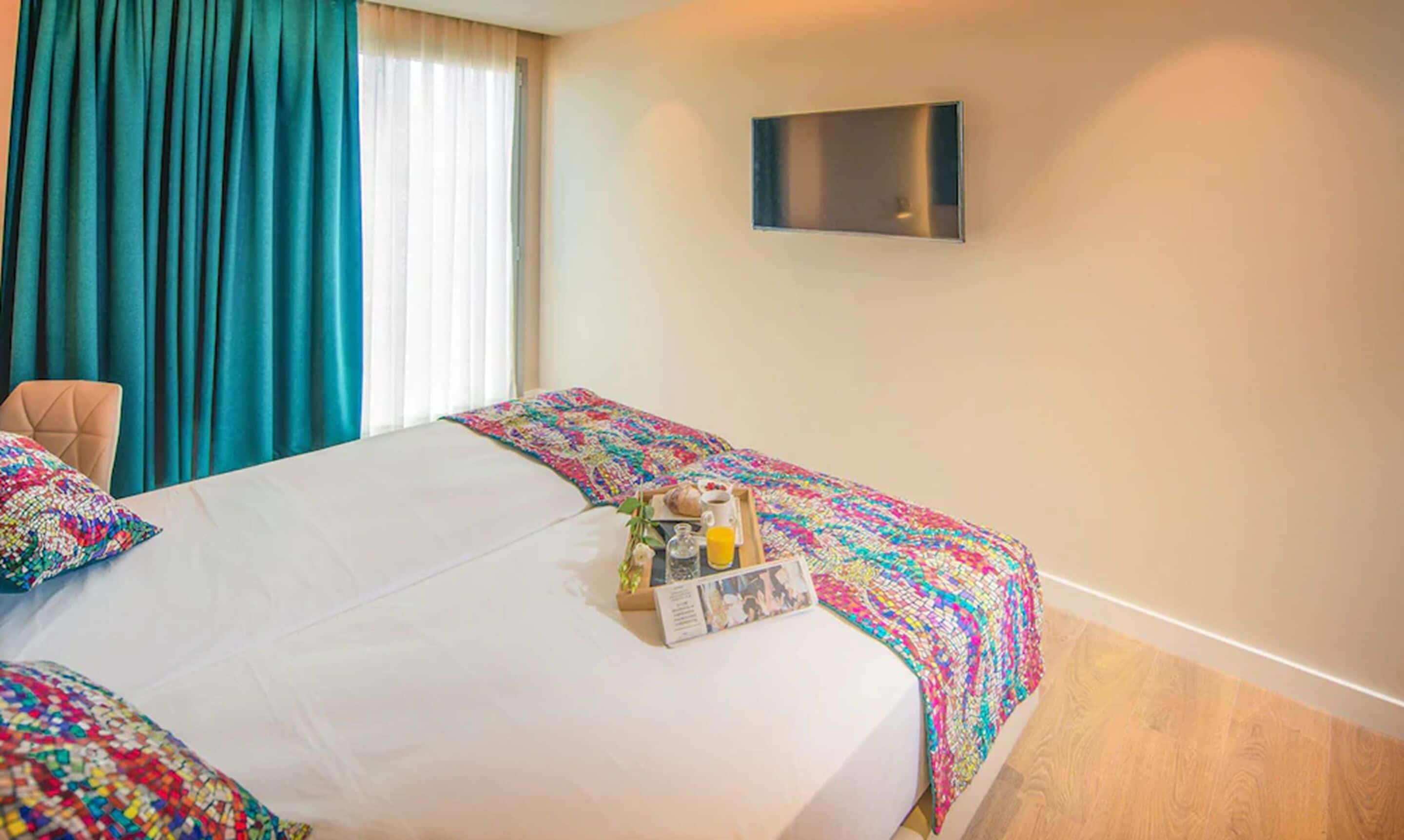 Habitación de hotel con cama, una silla, televisor y bandeja de desayuno sobre la cama.