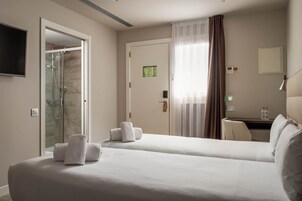 Habitación de hotel con dos camas, ducha, escritorio y televisión.