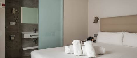Una habitación de hotel con cama, baño y puerta corredera hacia la zona de ducha.