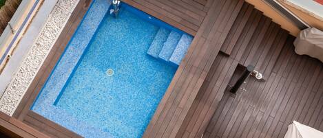 A rectangular swimming pool with a blue mosaic tile floor, surrounded by wooden decking.