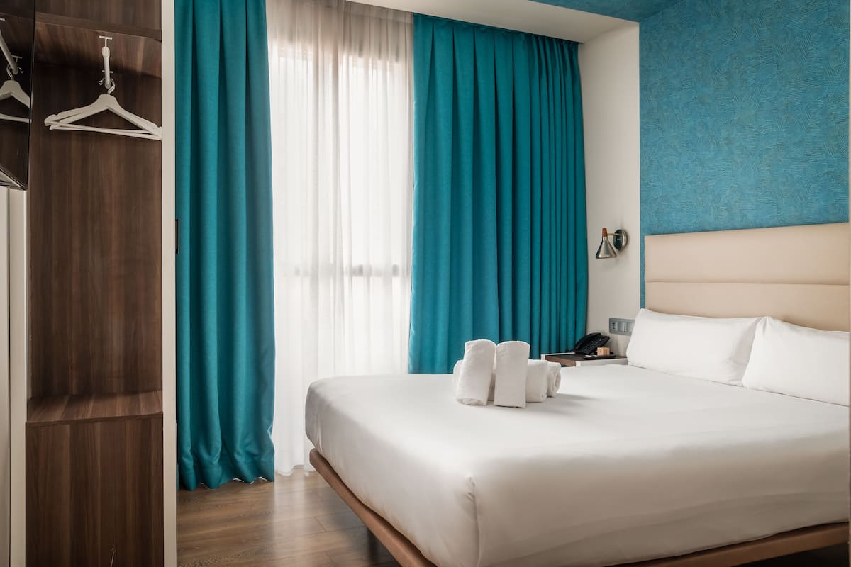 A hotel room with a bed, a wardrobe, and a window with curtains.