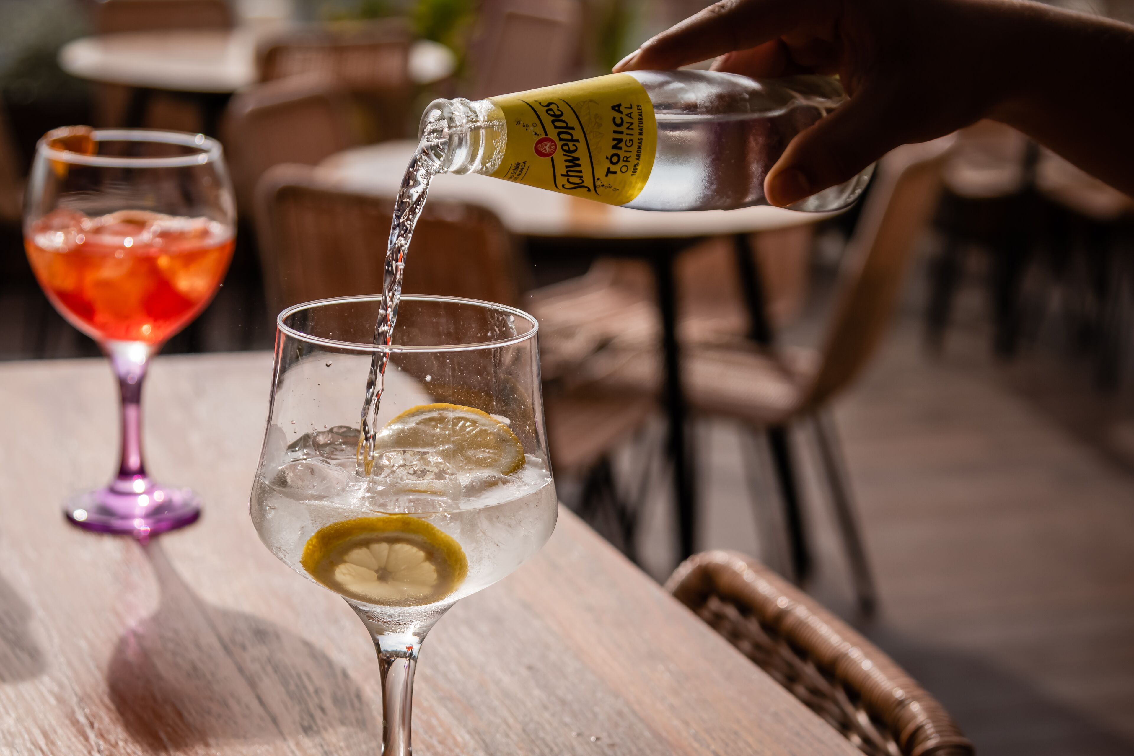 Une main verse une boisson d’une bouteille dans un verre, dans lequel on a mis une tranche de citron.