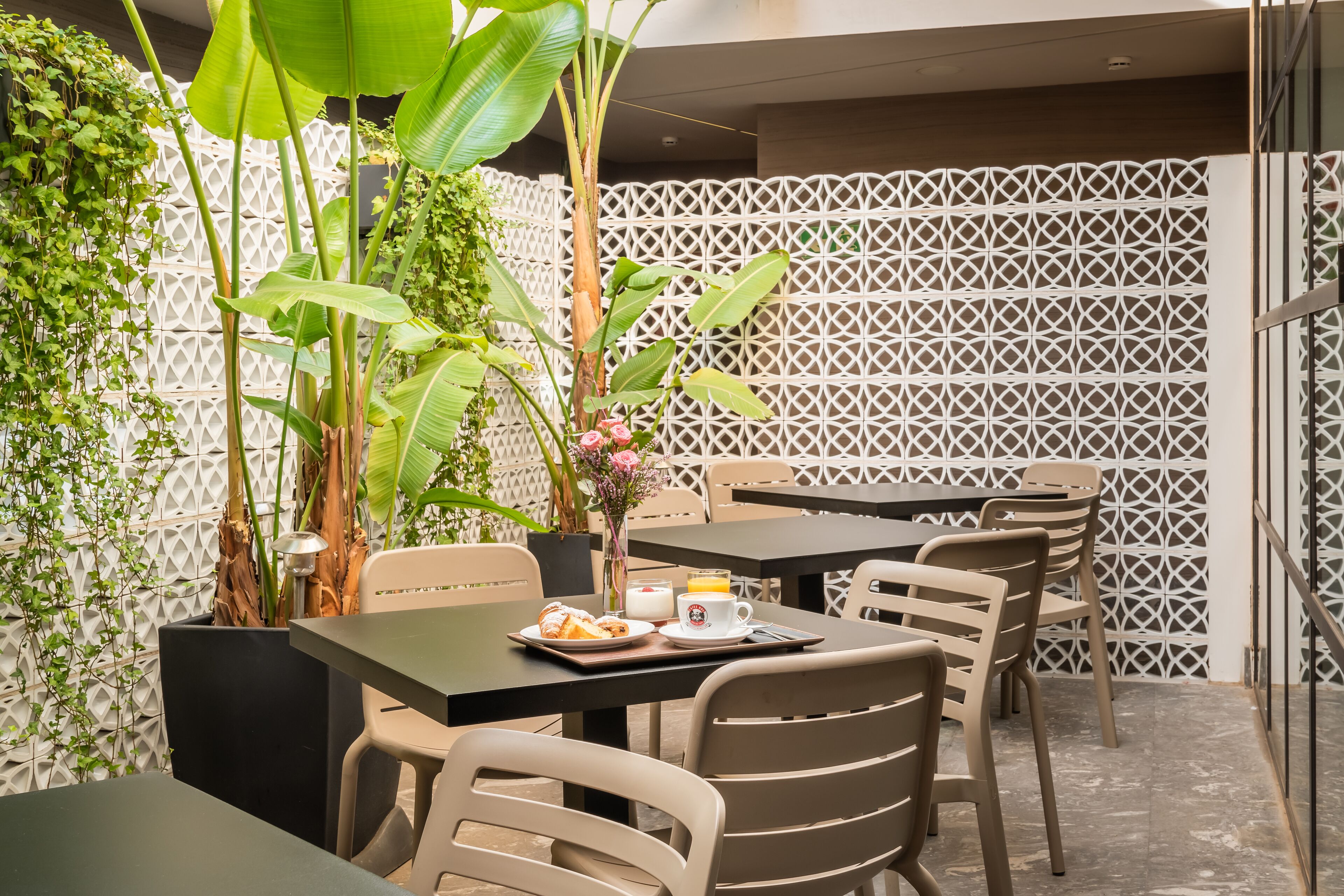 An outdoor dining area with tables and chairs, surrounded by plants and a decorative fence.