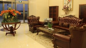 A lobby with a brown leather sofa set, a round wooden coffee table, and a floral arrangement on a side table.