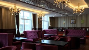 A restaurant with plush red seating, chandeliers, and a modern kitchen in the background.