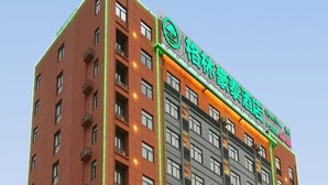 A multi-story hotel building with a modern design, featuring balconies on each floor and a prominent green sign with white text.