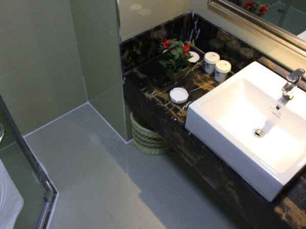 A bathroom with a white sink, a mirror, and a trash bin.