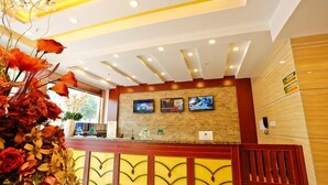 Una zona de recepción con un mostrador de madera, un jarrón grande con flores y un televisor montado en la pared.