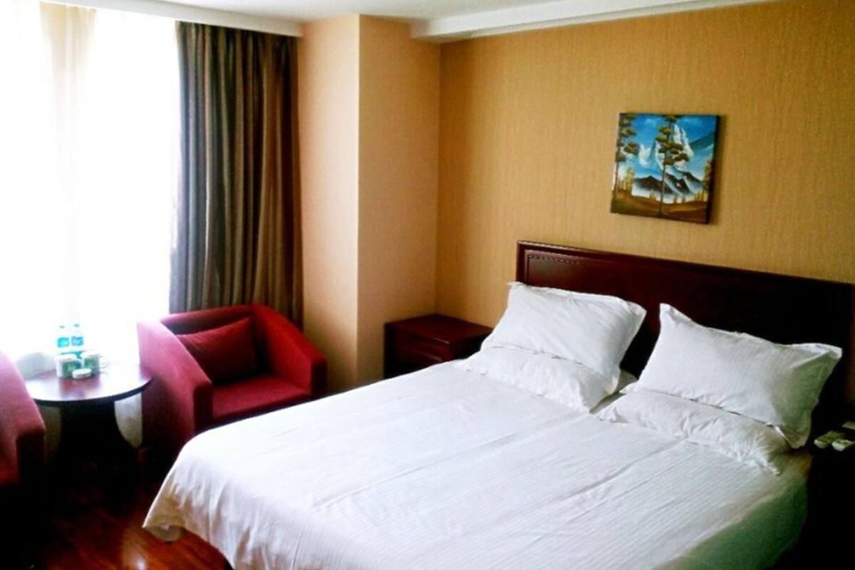 A hotel room with a large bed, a red armchair, a small table, and a painting on the wall.