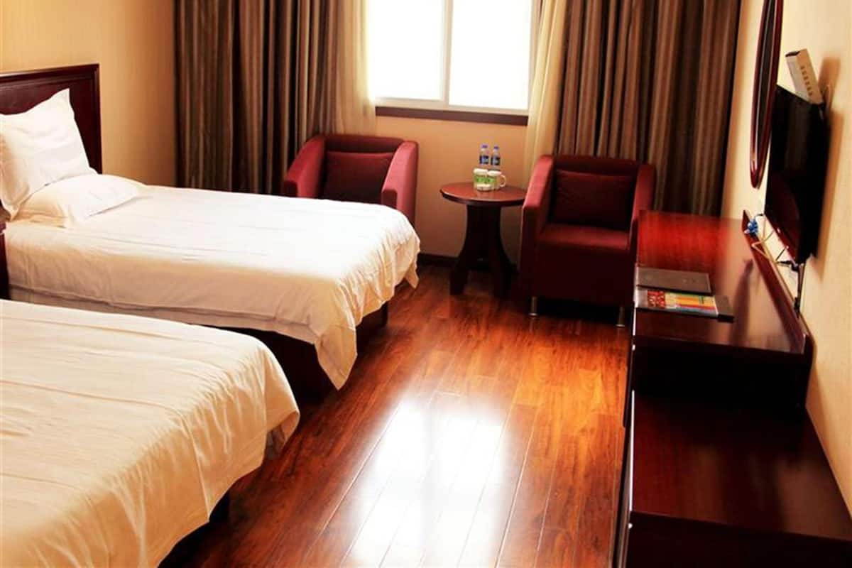 A hotel room with two beds, a small round table with a remote control, a red armchair, and a wooden dresser.