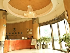 A hotel reception area with a wooden reception desk, a chandelier, and potted plants.