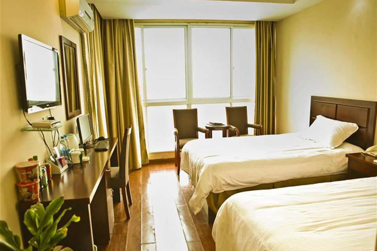 A hotel room with two beds, a desk with a computer, a chair, and a window with curtains.