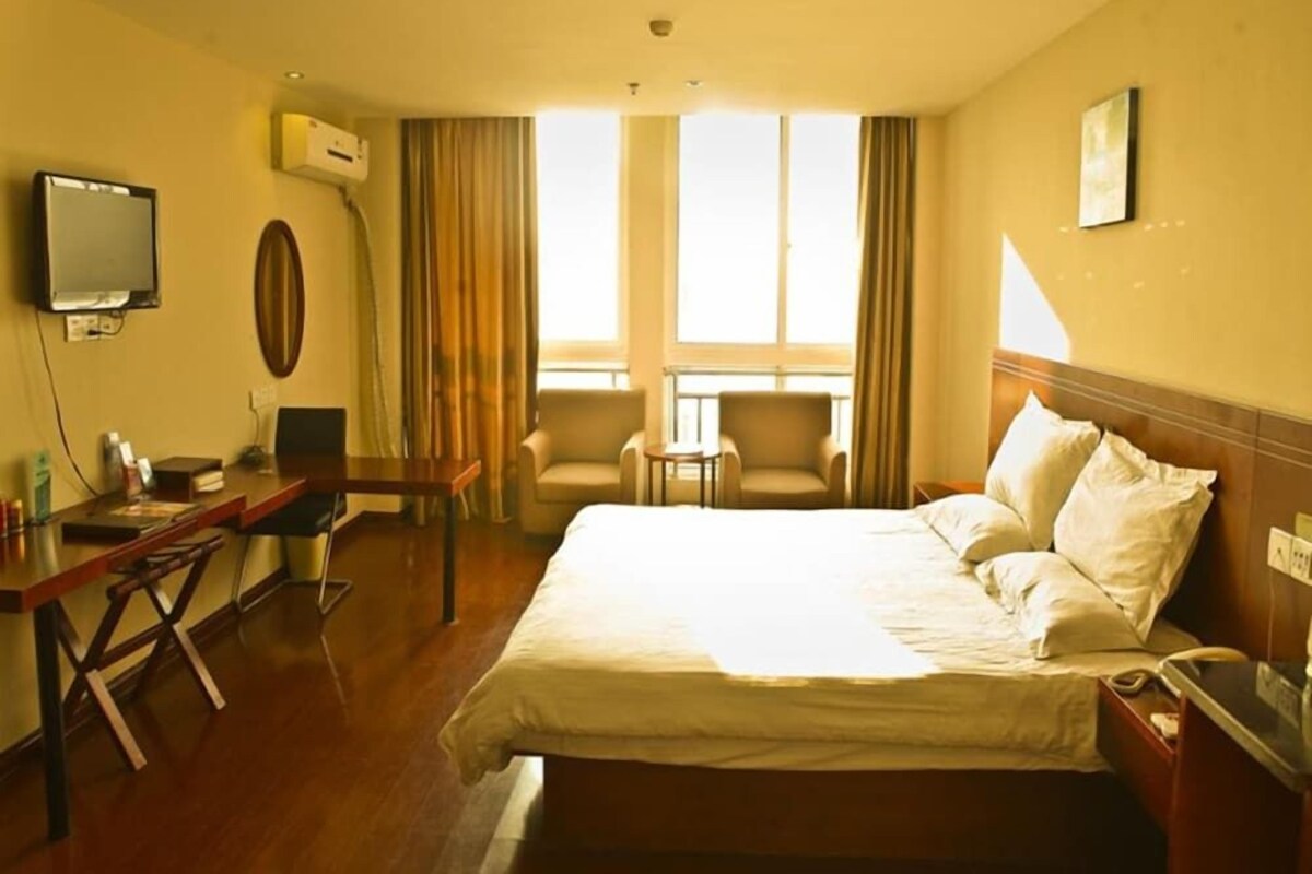Habitación de hotel con cama, dos sillones, un escritorio, televisor y ventana con cortinas.