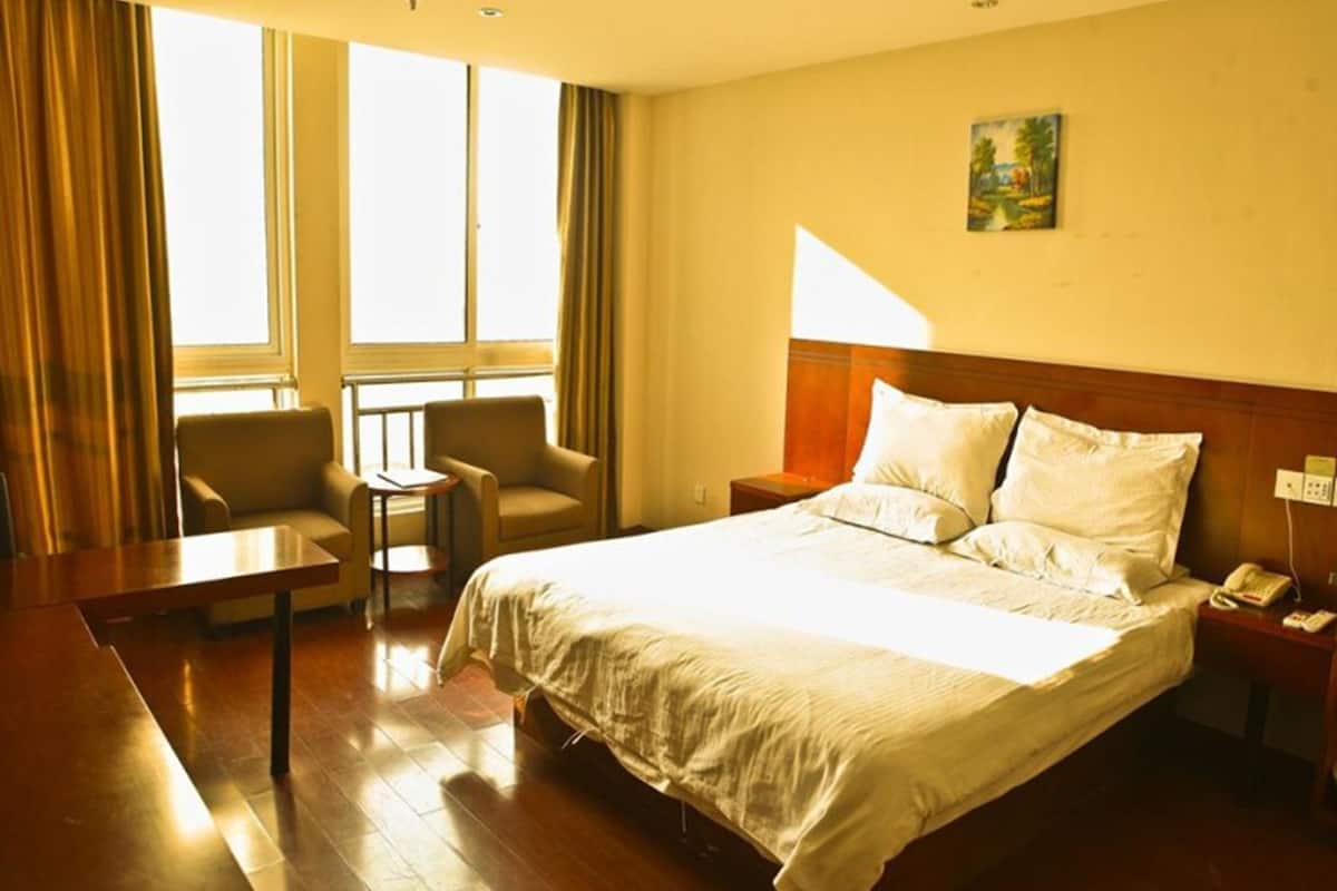 A hotel room with a large bed, a desk, two armchairs, a small table, and a painting on the wall.