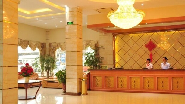 Um saguão de hotel com balcão de recepção, um candelabro e uma janela grande.