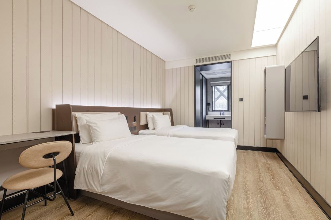 A hotel room with two beds, a desk, a chair, and a TV.