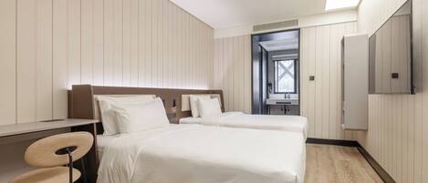 A hotel room with two beds, a desk, a chair, and a TV.