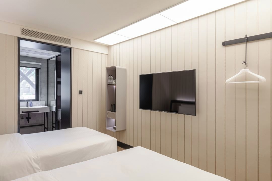 A hotel room with two beds, a TV, a wardrobe, and a hanging light fixture.