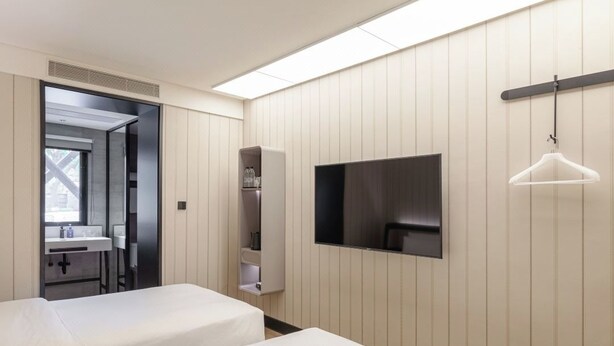 Ein Hotelzimmer mit zwei Betten, einem Fernseher, einem Kleiderschrank und einer Hängeleuchte.