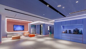 Eine moderne Hotelhalle mit Sitzgelegenheit, einer Rezeption und einem großen Bildschirm.