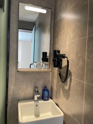A bathroom with a mirror, a sink, and a hairdryer mounted on the wall. - Hanting Hotel (Beijing)