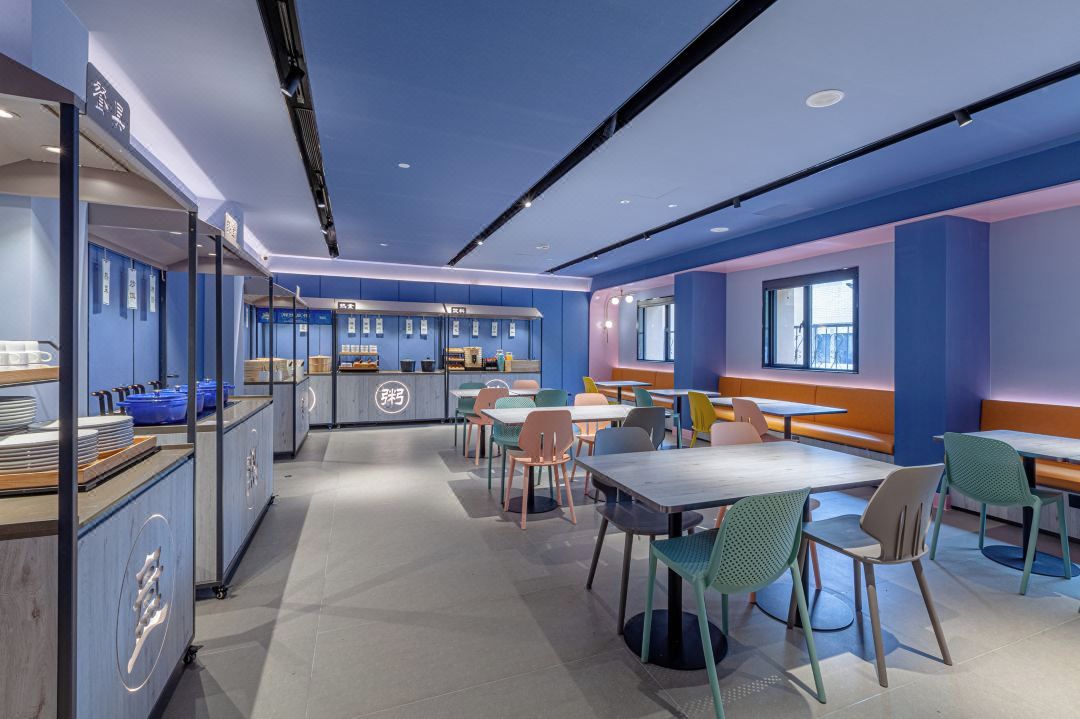 Un espace repas moderne avec des tables et des chaises, un comptoir où est affiché le menu, et un coin salon avec des bancs.