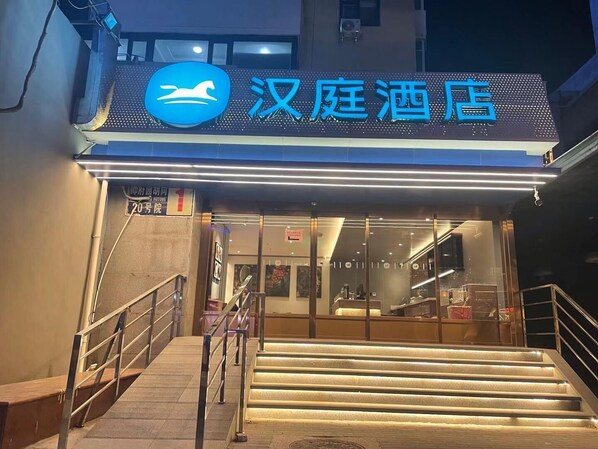 A hotel entrance with a sign in Chinese characters, a staircase leading up to the entrance, and a modern design with glass doors.