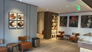 Eine moderne Hotelhalle mit Holzmöbeln, einer Kaffeemaschine und einem Bücherregal.
