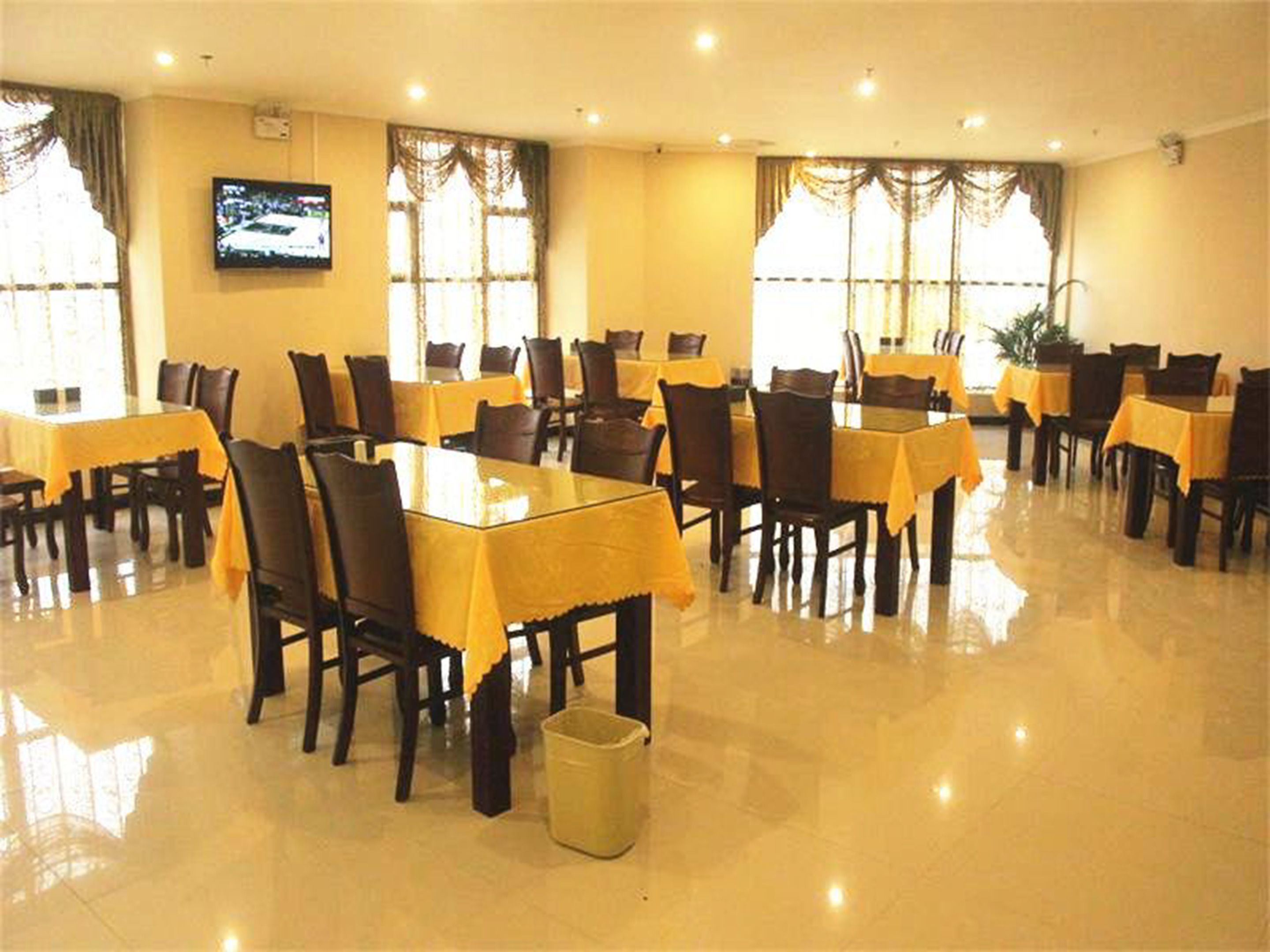 Un comedor con varias mesas y sillas, un televisor montado en la pared y ventanas grandes con cortinas.