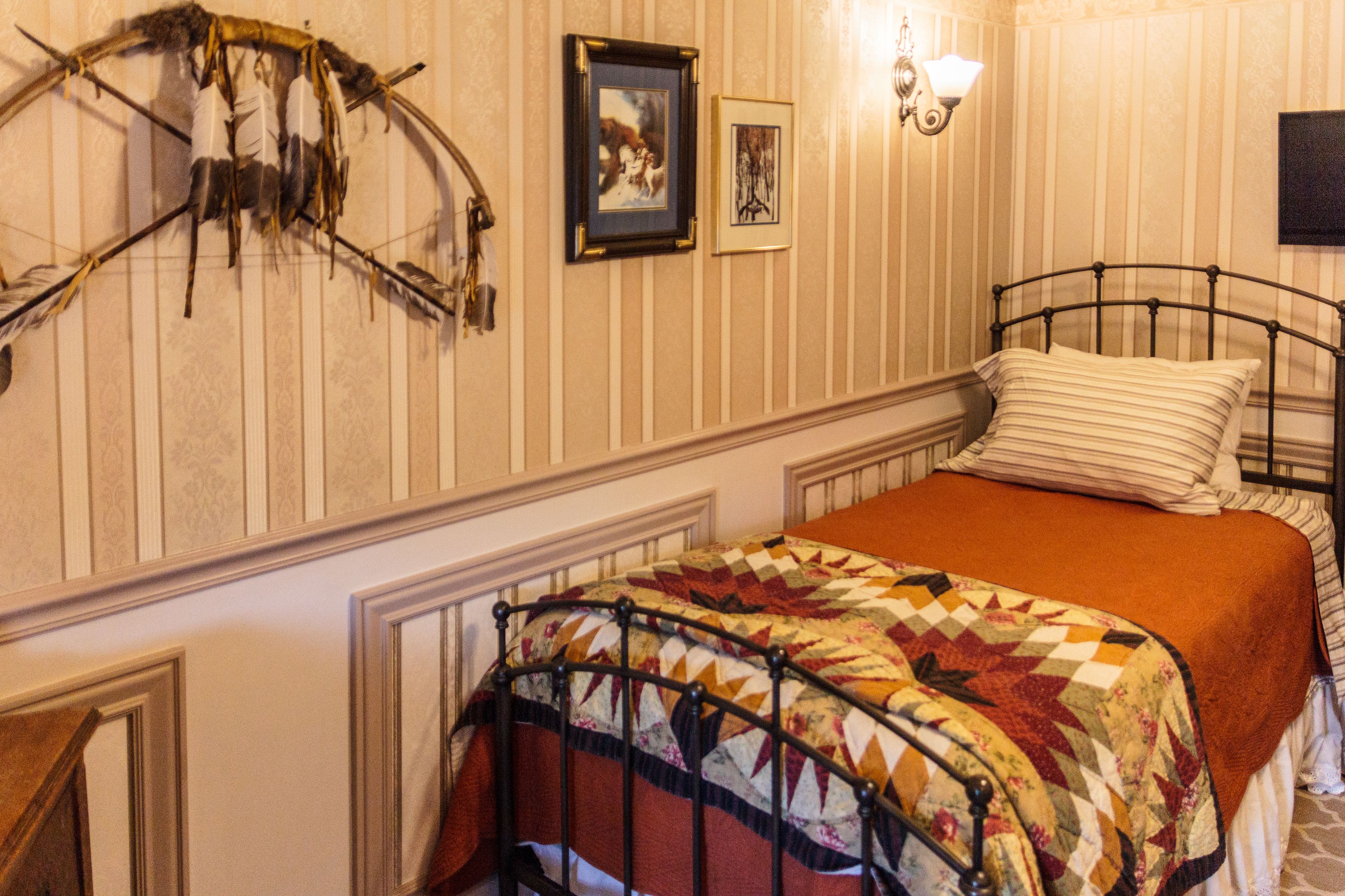 Un lit avec une courtepointe, un ensemble d’archerie fixé au mur et deux tableaux encadrés.